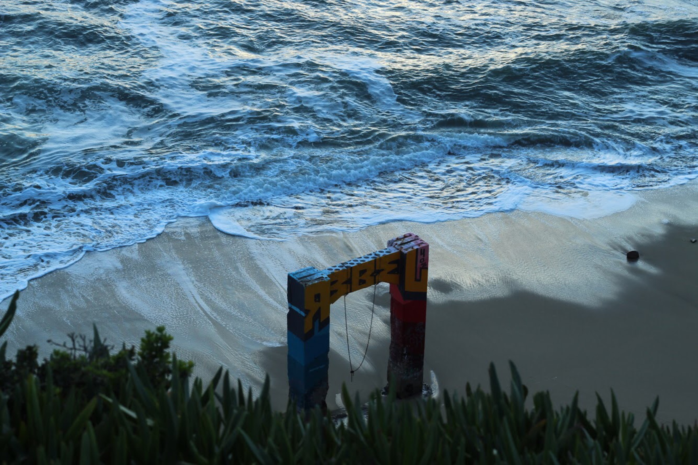 A colorful swing frame standing at the edge of a beach below rolling waves